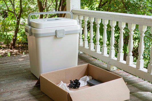 An open shipping box on a front porch beside a pet food bin with broken caster parts